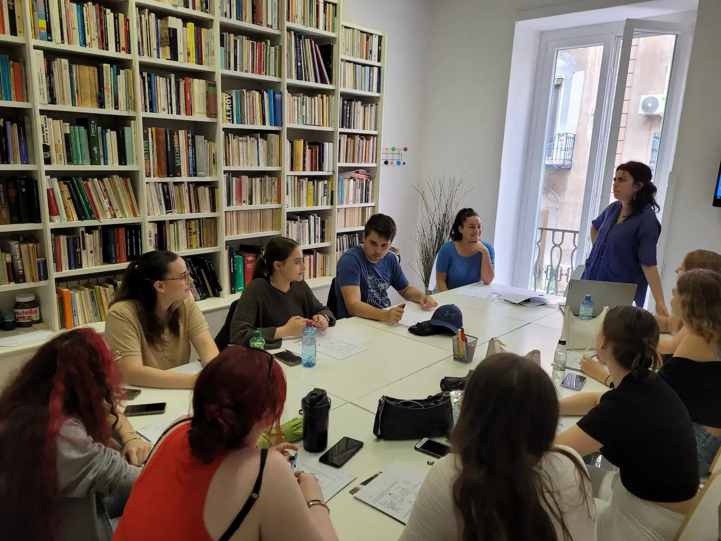 „Nemendur í tungumálatíma í Napólí sitja í kennslustofu við borð með kennara“